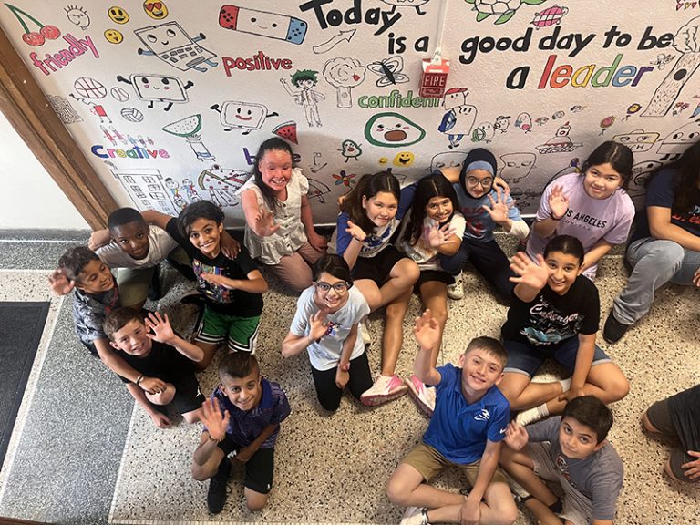 A group of Lindbergh Elementary 2024 Summer Discovery Program students pose in front of a mural they are creating.